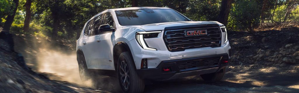 White GMC SUV driving on a dusty forest trail.