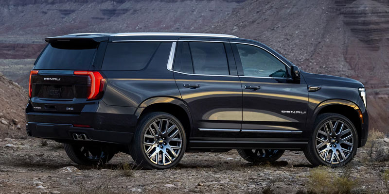 Side view of a black GMC Yukon Denali SUV parked on rocky terrain.