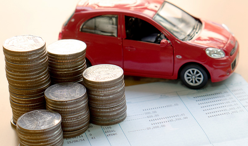 Stack of coins next to a red toy car on financial documents symbolizing car financing and budgeting.