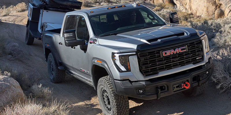 2026 GMC Sierra HD pickup truck towing a trailer on an off-road trail.